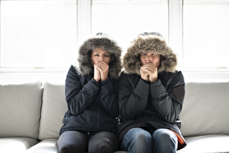 Man and woman sitting on a couch with winter coats on.
